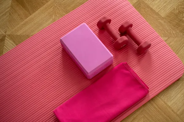 Pink exercise equipment; dumbbells, yoga mattress, towel on a wood floor