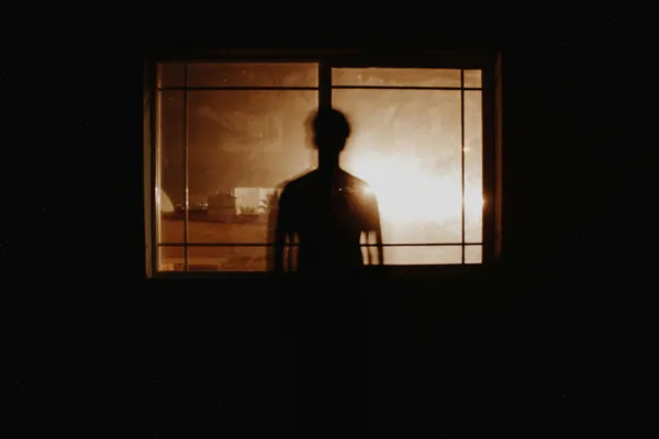 Silhouette of a person in front of a window in yellow lighting