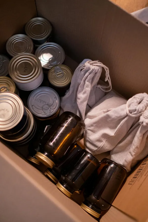 Canned food, jars, and sacs for donation in a cardboard box.