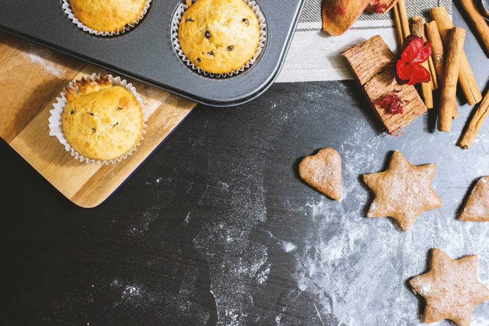 A countertop dusted with powdered sugar, with muffins and cookies